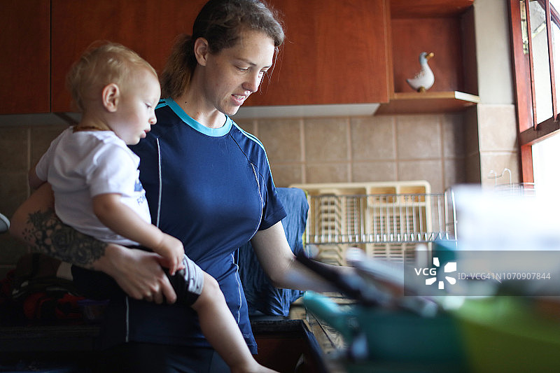 妈妈抱着她的儿子在洗碗。图片素材