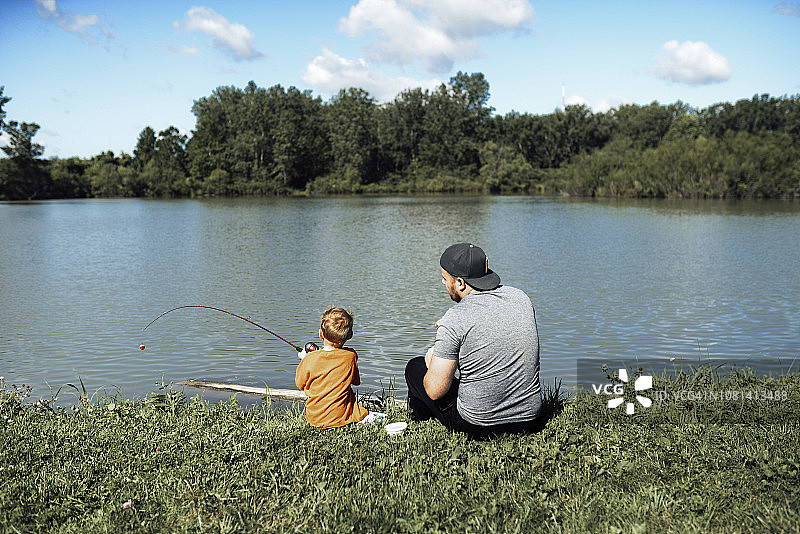 后视图钓鱼时，儿子与父亲坐在湖边对着天空图片素材