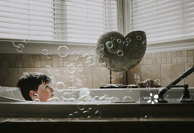 男孩在浴缸洗澡时看泡泡图片素材