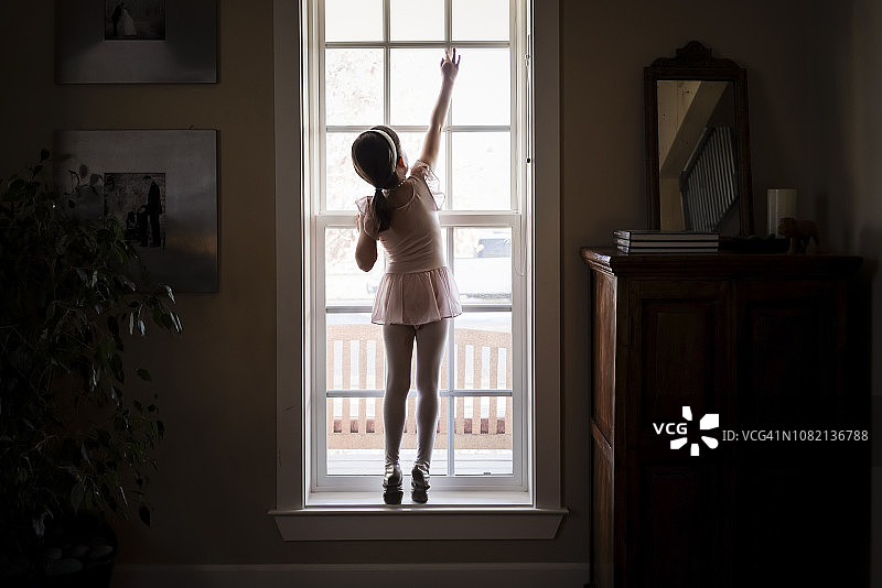 后视图的女孩在芭蕾服装关闭窗户在家里图片素材
