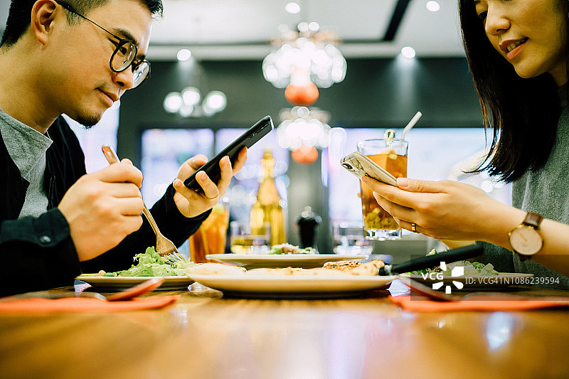 年轻情侣在餐厅吃饭时使用智能手机，忽视对方图片素材