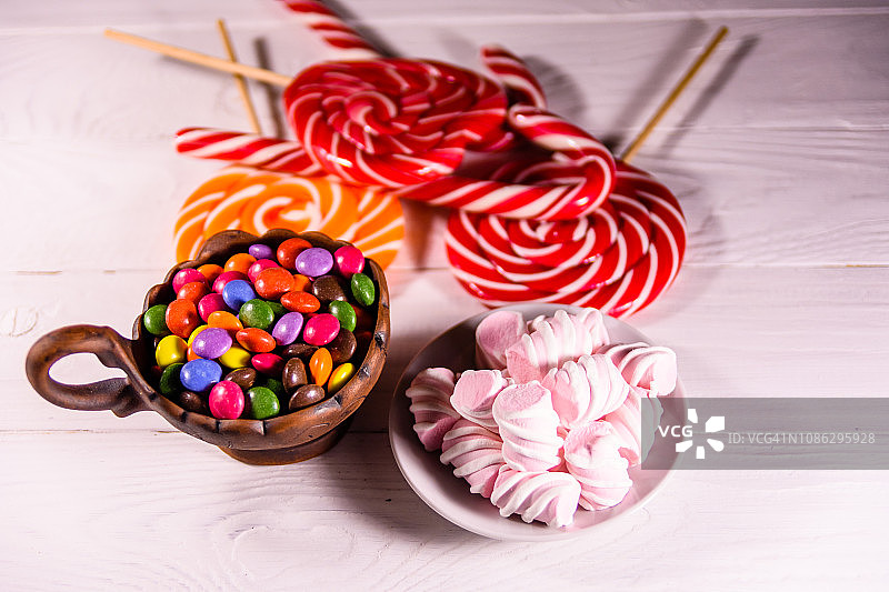 瓷碗，木桌上放着彩色糖果、棒棒糖和棉花糖图片素材