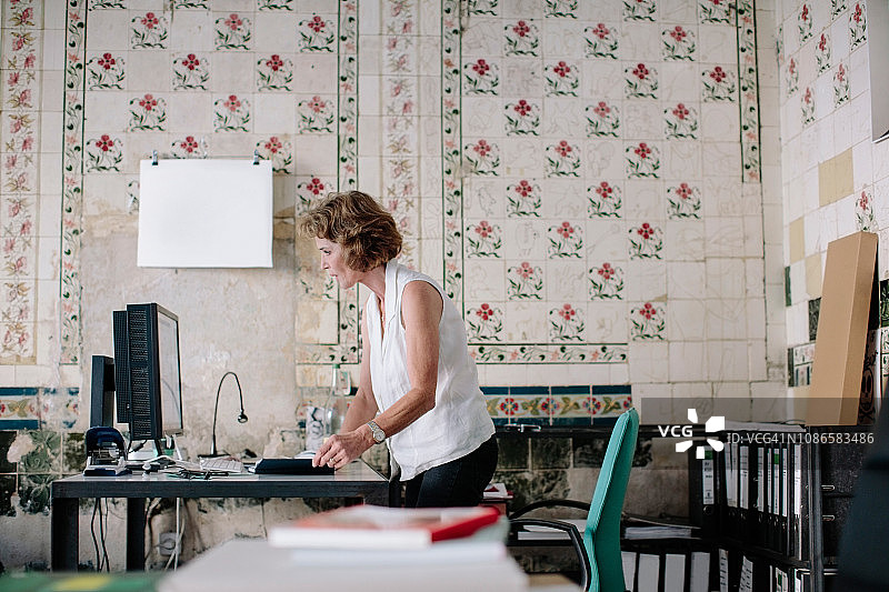 在设计室里，一位高级女商人站在日记本旁看着台式电脑图片素材