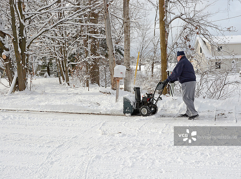 成熟的男人在冬天使用吹雪机图片素材