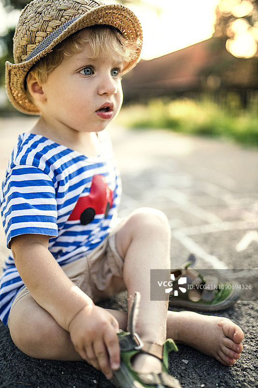 一个蹒跚学步的小男孩坐在街上脱鞋图片素材