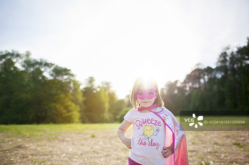 在阳光明媚的日子里，女孩穿着斗篷和面具站在晴朗的天空下图片素材