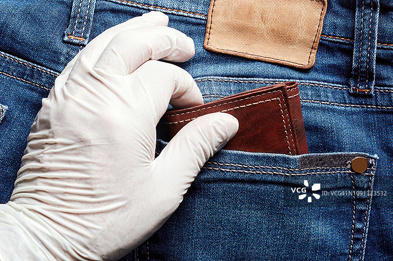 一个戴着白色乙烯基手套的小偷从牛仔裤的后口袋里偷了一个钱包。近距离观看扒窃。图片素材