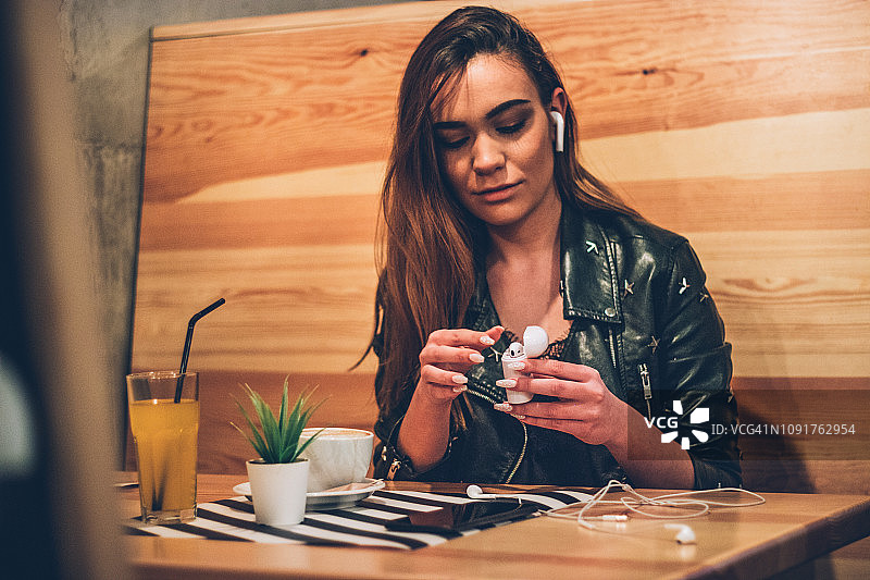 一个戴着无线耳机的年轻女子坐在咖啡馆里图片素材