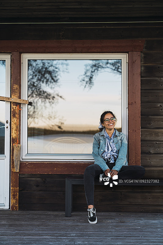 一个快乐的年轻女子坐在木屋的阳台上图片素材