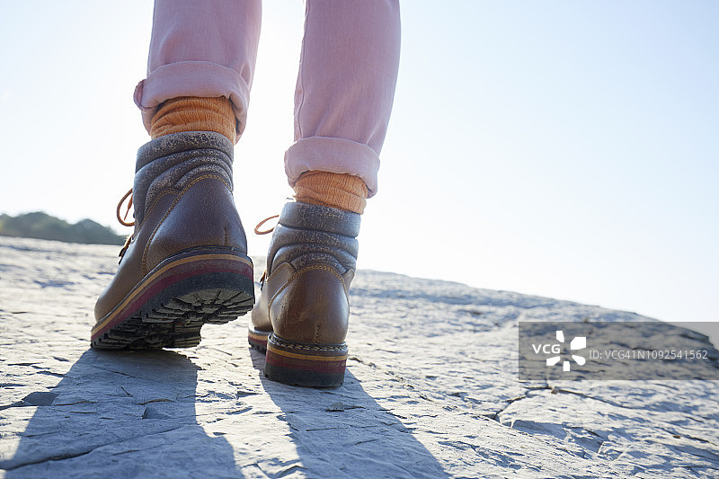 穿着登山靴的女人在海边的岩石上行走图片素材
