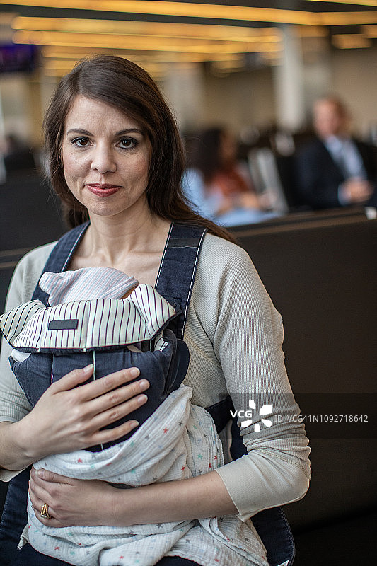 在机场大厅，母亲在摇篮里抱着孩子。图片素材
