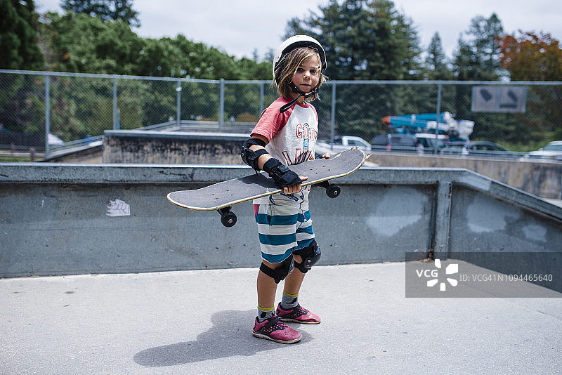 女孩手拿滑板站在公园的运动坡道上的肖像图片素材