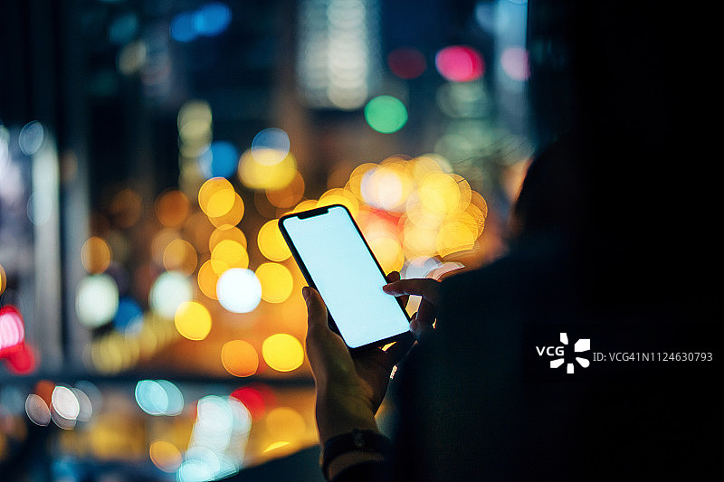 晚上，香港市中心灯火通明，一名女性用智能手机发短信图片素材