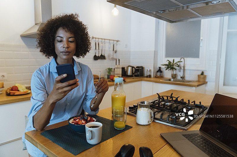 一个女人在厨房里用着智能手机吃早餐图片素材