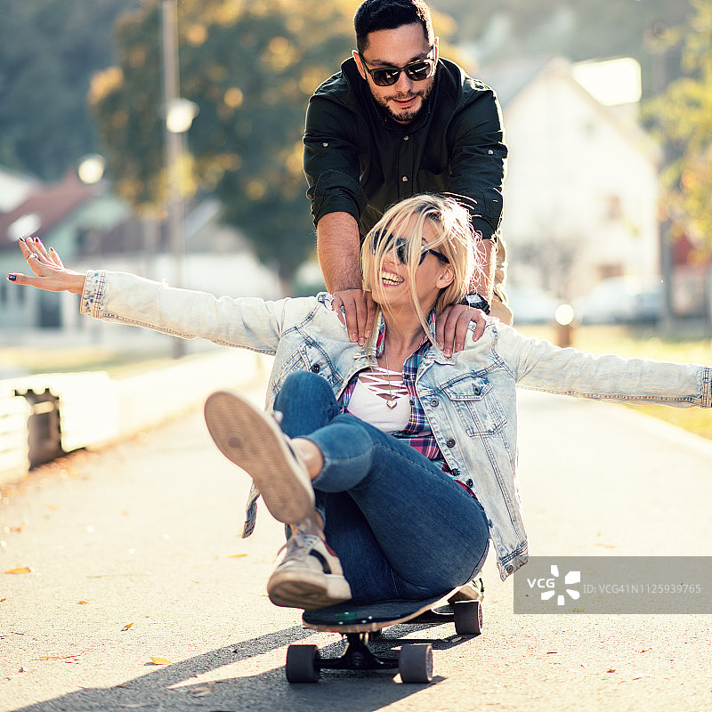 一个年轻人用滑板推他的女朋友图片素材