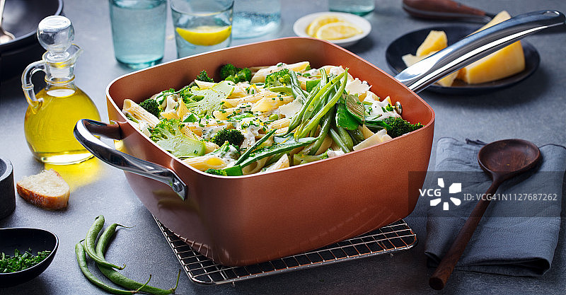 铜炖锅里的绿色蔬菜和奶油酱意大利面。灰色背景。图片素材