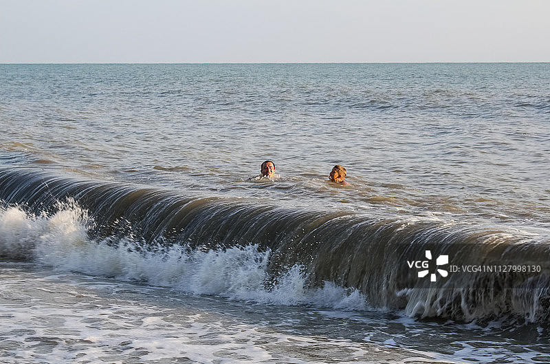 一个男人和一个少年在大海里游泳，在大浪中图片素材