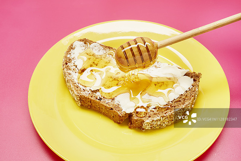 蜂蜜勺把蜂蜜滴在黄色盘子上的一片面包上图片素材