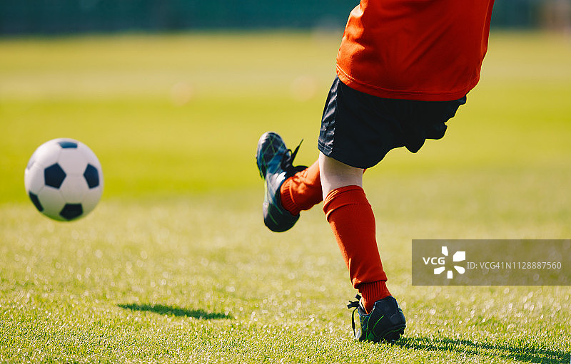 年轻的足球运动员在足球场上踢球。穿着红色运动衫，黑色短裤，红色足球袜和黑色球鞋的男孩。在草地体育场踢足球图片素材