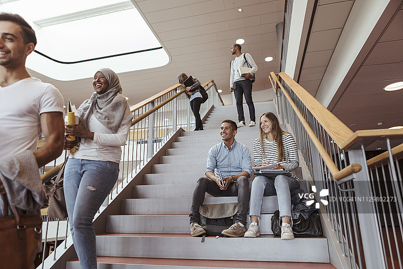 微笑的学生坐在台阶上看着大学里的朋友图片素材