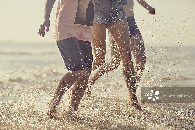 在夏日家庭海滩旅行中，一家人欣喜若狂地跑过大海图片素材
