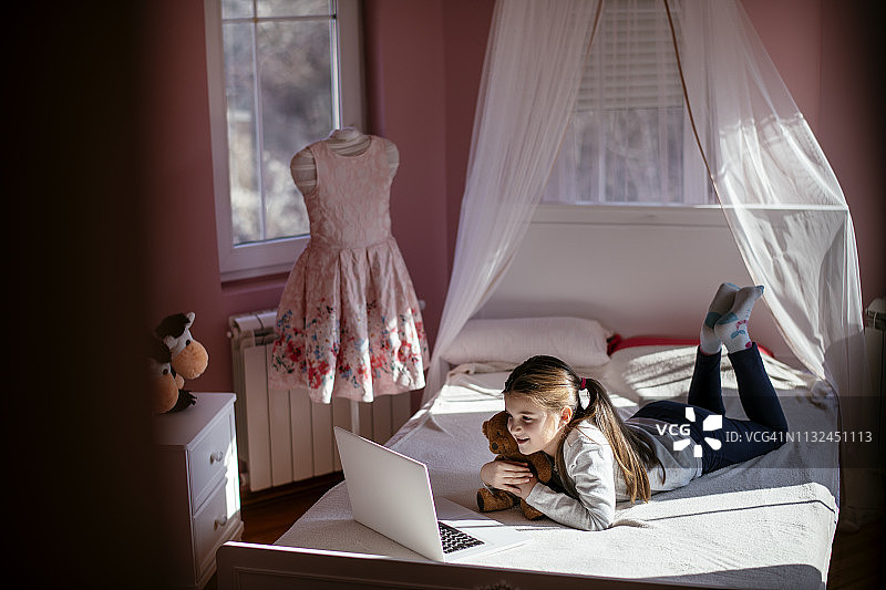 微笑的小女孩在床上使用笔记本电脑。图片素材