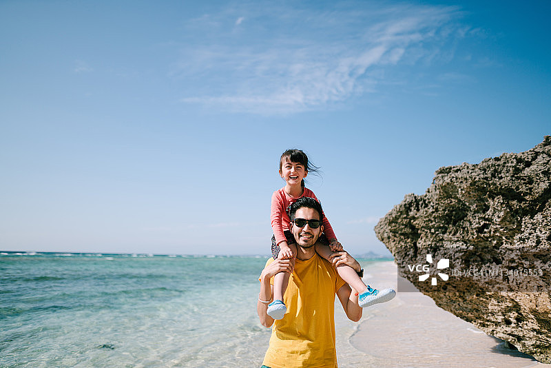 在日本冲绳的热带海滩上，父亲背着学龄前的女儿图片素材