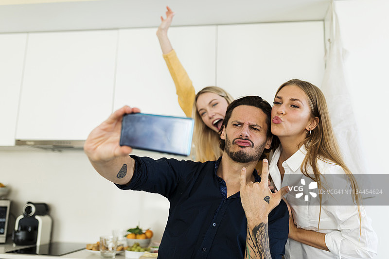 朋友们开心地站在厨房里，用他们的智能手机拍照图片素材