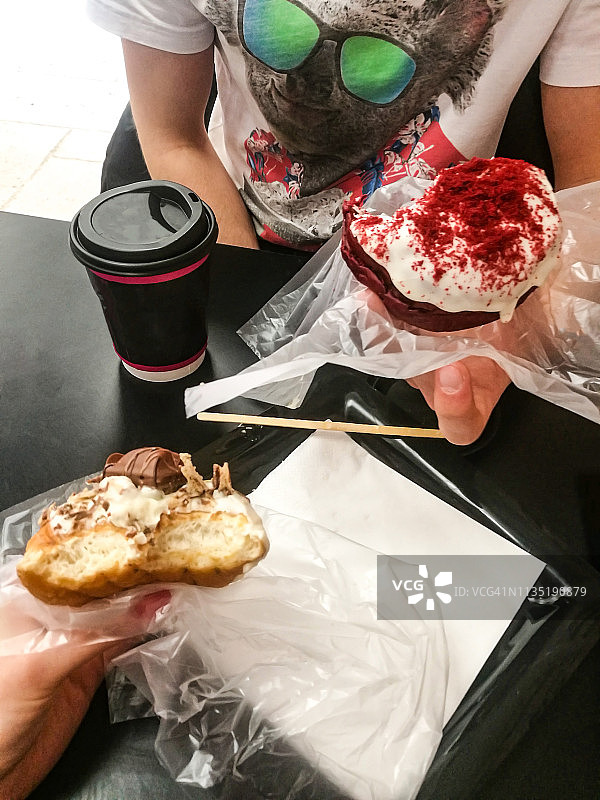 木桌上放着甜甜圈和咖啡，一个男人拿着咖啡图片素材