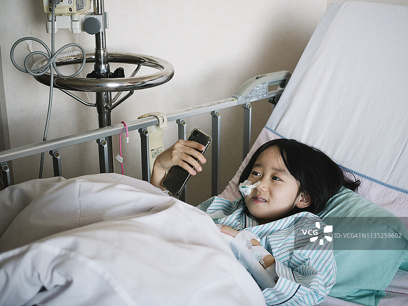 住院的日本女孩在床上看智能手机屏幕图片素材