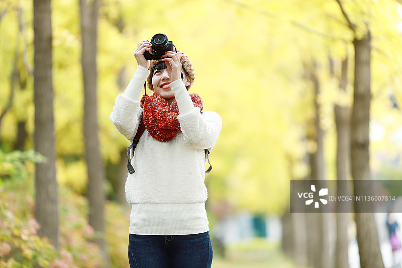 年轻女子在秋天的公园里用相机拍照图片素材