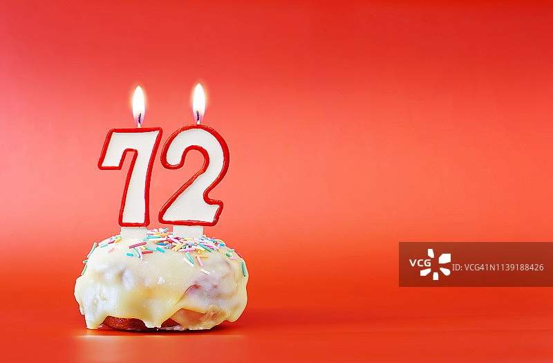 七十二岁生日。纸杯蛋糕，上面有燃烧着的白色蜡烛，形状是数字72。鲜艳的红色背景与复制空间图片素材