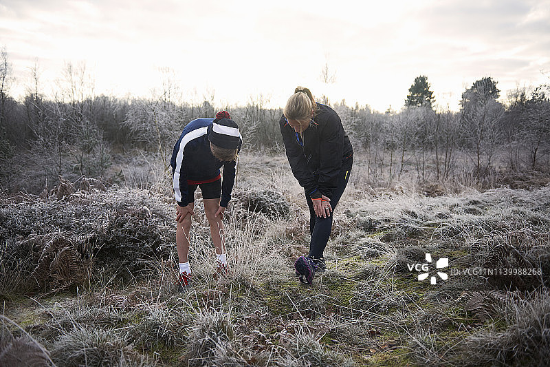 母亲和儿子在霜冻的草原上，手放在膝盖上，伸伸腿向下看图片素材