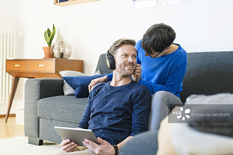 一对戴着耳机的休闲情侣在他们现代的客厅里放松在沙发上图片素材