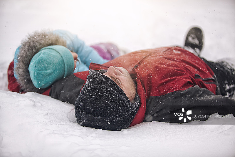 父亲和女儿戴着针织帽躺在雪地里图片素材