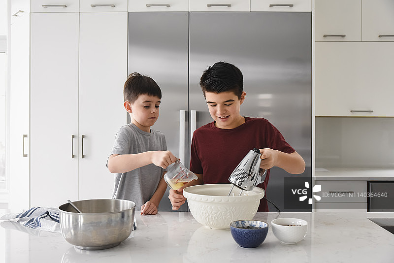 两个男孩在一个现代化的厨房里使用搅拌机和量杯图片素材