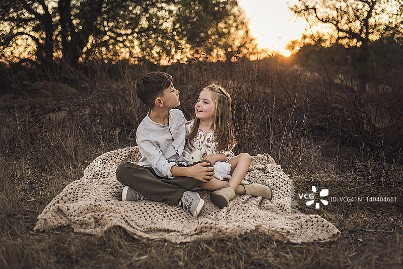 日落时分，年轻的女孩和男孩坐在加州田野的毯子上图片素材