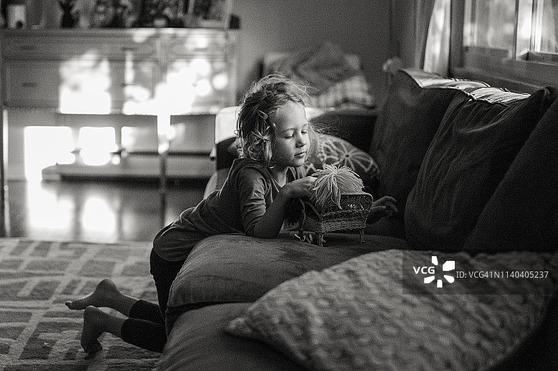 一个光着脚的小女孩在一片窗光中玩她的洋娃娃图片素材