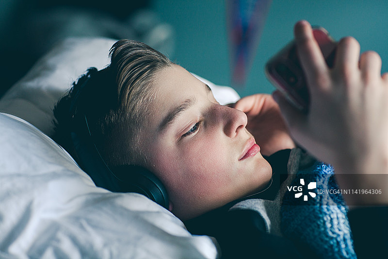 男孩躺在床上通过无线耳机听音乐图片素材