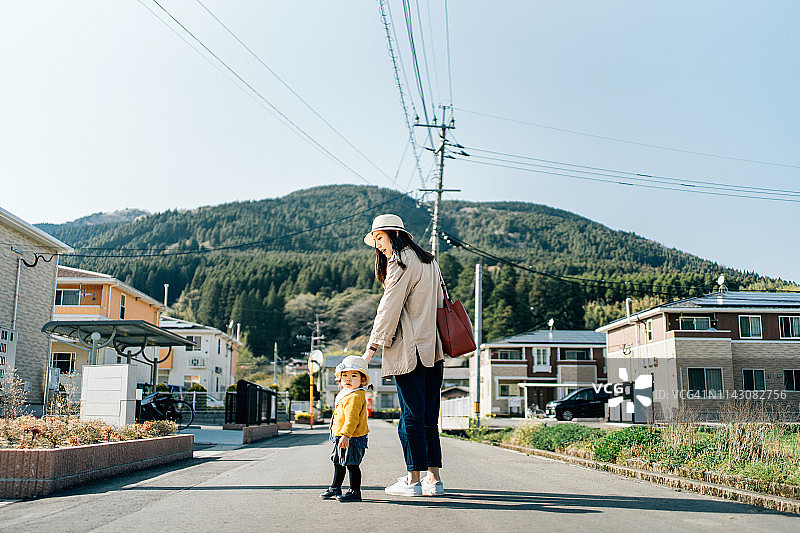 在一个阳光明媚的日子里，可爱的小女孩戴着草帽，与母亲手牵着手走在乡村的小镇上图片素材