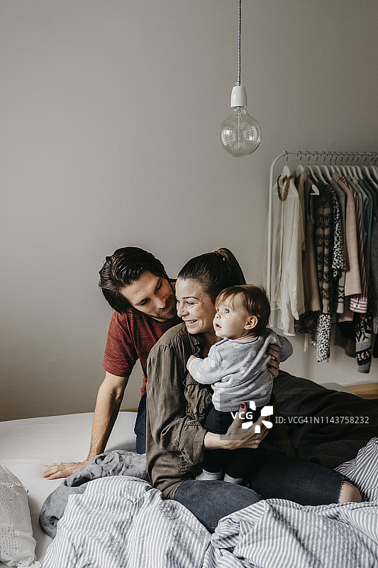一个幸福的家庭，女婴坐在家里的床上图片素材