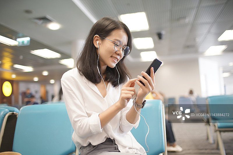 女青少年在机场等待时用智能手机听音乐图片素材