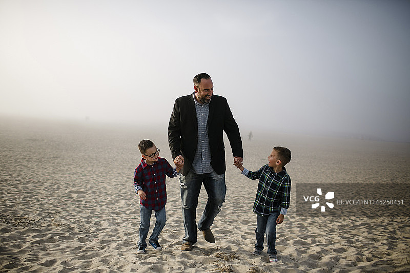 在雾蒙蒙的天气里，微笑的父亲和可爱的儿子们在海滩上散步图片素材