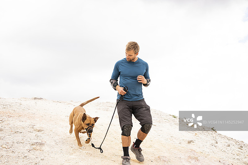 在多云的天空下，带着狗在山上散步的人图片素材