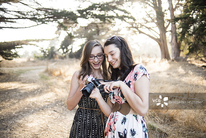 快乐的姐妹看着相机里的照片，而站在森林的树木图片素材