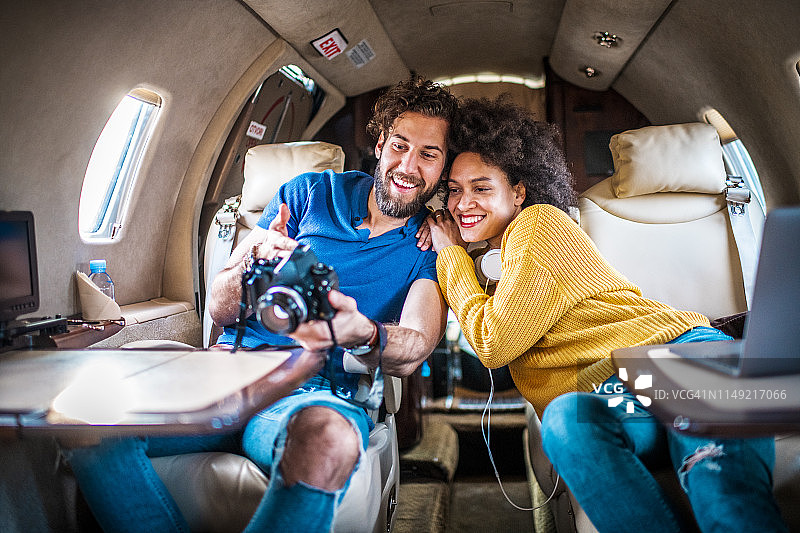 一对年轻夫妇坐在私人飞机上用单反相机看一些照片，享受在一起的乐趣图片素材