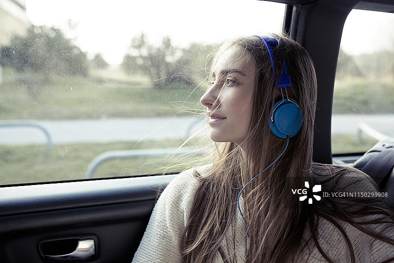 年轻女子，头发被风吹乱，戴着耳机坐在车里图片素材