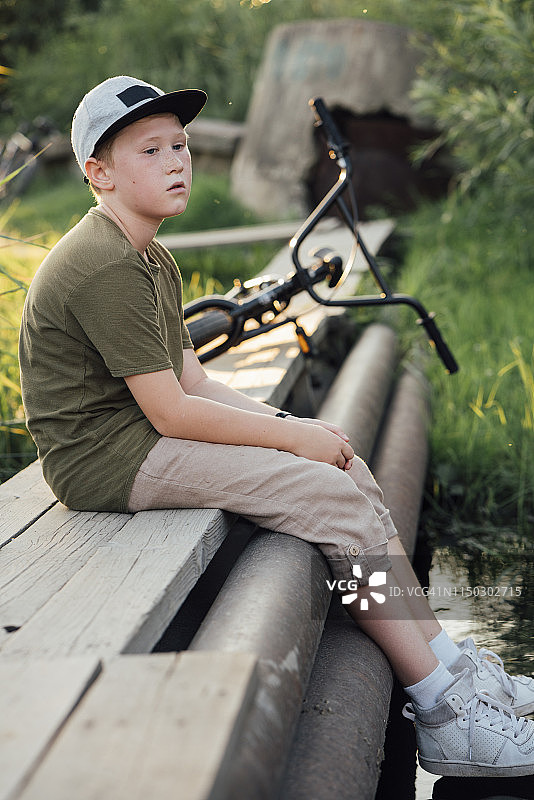 严肃的男孩骑着小轮车坐在木板路上图片素材