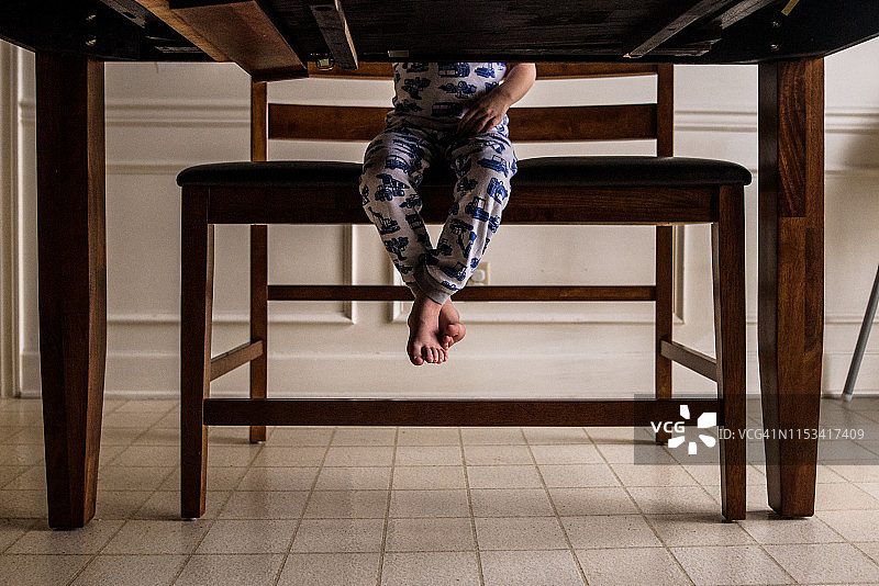 从桌子下面可以看到一个小男孩的脚悬在高高的长凳上图片素材