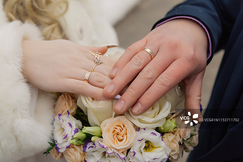 新娘和新郎的手与戒指在婚礼花束。婚姻的概念图片素材